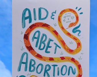 May include: A hand-held art print with the words "AID & ABET ABORTION" in teal lettering. A stylized orange and red snake winds through the text. Additional text includes "WITH LOVE & CARE" and "WITH FIGHT & FURY".