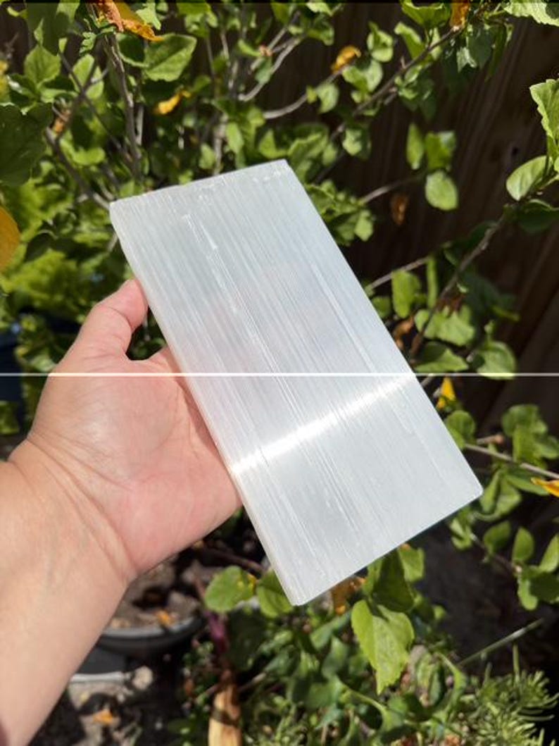 May include: A rectangular slab of white selenite crystal with a fibrous, translucent texture and a smooth, flat surface. The stone displays natural vertical striations and a pearlescent sheen that reflects light across its elongated, flat form.