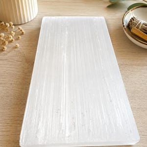 Op de afbeelding: Een rechthoekige plaat van witte selenietkristal met een glad, plat oppervlak en een vezelige, doorschijnende textuur. Het kristal heeft natuurlijke verticale strepen over de lengte, wat zorgt voor een subtiel glinsterend uiterlijk.