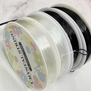 May include: Two spools of clear elastic string, one black and one white, labeled "CRYSTAL STRING 0.7mm 15M".