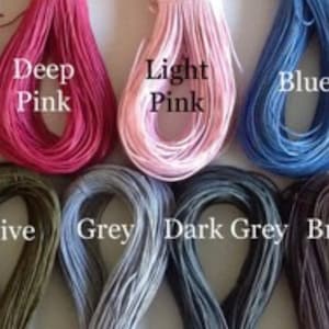 May include: A collection of spools of thread in various colours, including purple, white, red, deep pink, light pink, blue, cyan blue, yellow, turquoise, lime green, olive, grey, dark grey, brown, and black.