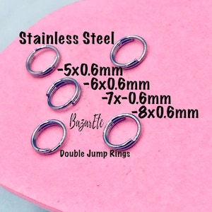 Peut inclure: Quatre anneaux de saut doubles en acier inoxydable de différentes tailles, 5 mm, 6 mm, 7 mm et 8 mm, tous d'une épaisseur de 0,6 mm. Les anneaux sont sur une surface rose avec le texte "Stainless Steel" et "Double Jump Rings" écrit en dessous.