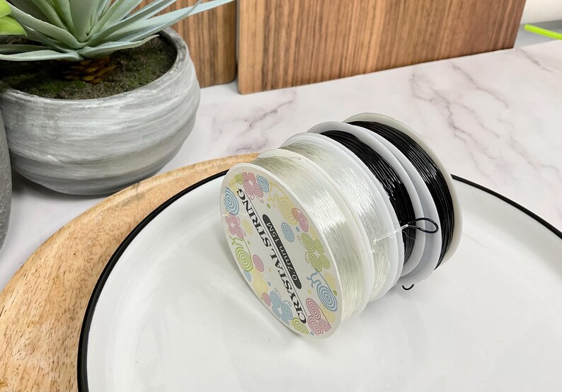 May include: Close-up of a spool of clear elastic string with a colorful label that reads "Crystal String Best Quality".