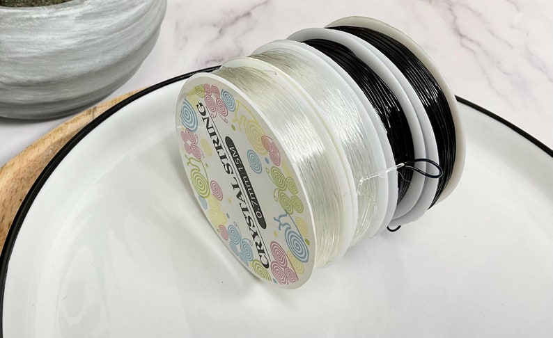 May include: Two spools of clear elastic string, one black and one white, labeled "CRYSTAL STRING 0.7mm 15M".