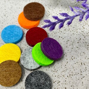 Peut inclure: Assortiment de pastilles de diffuseur en feutre de différentes couleurs, dont le marron, l'orange, le rouge, le bleu, le jaune, le gris, le vert, le violet et le noir. Les pastilles sont rondes et ont une texture douce et duveteuse.