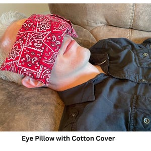 May include: A red eye pillow with a white paisley pattern is placed over a person's eyes. The pillow is made of a cotton cover. The text "Eye Pillow with Cotton Cover" is at the bottom of the image.