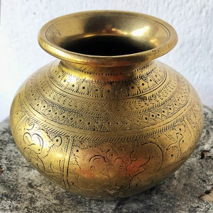 Puede incluir: Un jarrón de latón dorado con intrincados diseños grabados. El jarrón tiene un cuerpo redondo y una boca ancha.