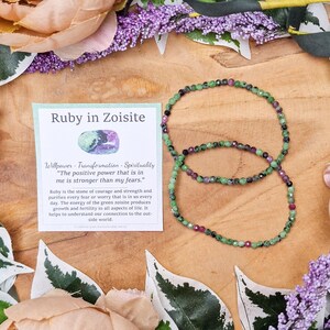 Könnte beinhalten: Ein grünes und rotes Edelstein-Armband mit einer Karte, auf der "Ruby in Zoisite" steht und die Eigenschaften der Steine beschrieben werden. Die Karte enthält auch das Zitat "Die positive Kraft, die in mir ist, ist stärker als meine Ängste."