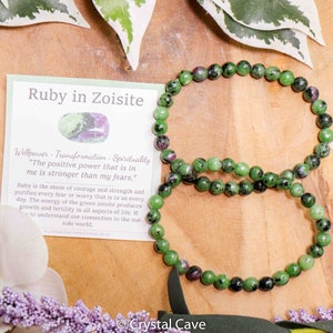 Pode incluir: Um bracelete de rubi em zoisita verde e rosa com um cartão que diz "Ruby in Zoisite" e "Willpower - Transformation - Spirituality" com uma citação sobre o poder positivo que está dentro de nós.