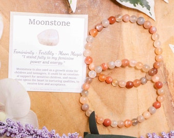 May include: A moonstone bracelet with a card that reads "Moonstone: Femininity, Fertility, Moon Magic. "I stand fully in my feminine power and energy." Moonstone is also used as a growth stone for children and teenagers. It could be an emotional support for sensitive children, and moonstone opens the heart to nurturing qualities, to receive love and acceptance."