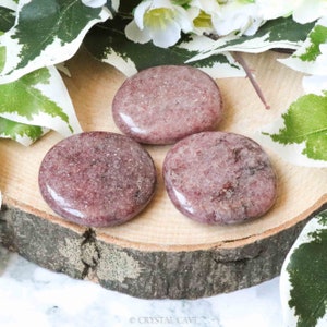 May include: Three smooth, polished red jasper stones, each with a unique pattern of swirling red and white veins. The stones are arranged on a wooden surface.