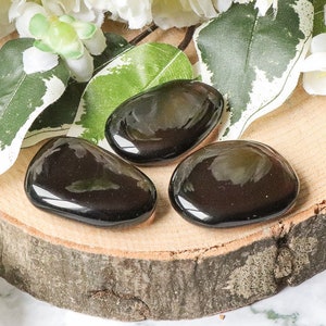 Peut inclure: Trois pierres d'obsidienne noires lisses sur une surface en bois. Les pierres sont polies et ont une finition brillante.