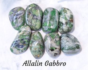 May include: A collection of polished Allalin Gabbro stones, showcasing a mix of green, gray, and white hues. The stones have a smooth, rounded shape and are arranged on a white surface. The text "Allalin Gabbro" is visible.