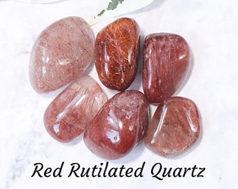 May include: Six tumbled red rutilated quartz stones. The stones are translucent with red and gold inclusions. Red rutilated quartz is a variety of quartz that contains inclusions of rutile, a mineral that gives the stone its red color.