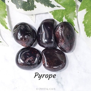Puede incluir: Cinco piedras de granate piropo pulidas, cada una con un color rojo intenso y una superficie lisa y pulida. Las piedras están dispuestas sobre un fondo blanco.