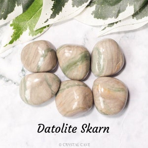 May include: A collection of six smooth, light brown and green datolite skarn tumbled stones. The stones have a natural, polished finish and are arranged on a white surface.