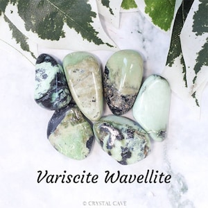 May include: A collection of six smooth, polished variscite wavellite stones. The stones are a mix of light green and dark green with black flecks. The stones are arranged on a white surface.
