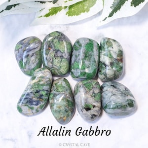 May include: A collection of polished Allalin Gabbro stones, showcasing a mix of green, gray, and white hues. The stones have a smooth, rounded shape and are arranged on a white surface. The text "Allalin Gabbro" is visible.