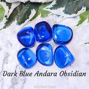 Puede incluir: Seis piedras pulidas de color azul oscuro, conocidas como Obsidiana Andara, sobre una superficie de mármol blanco. Las piedras son lisas y pulidas, de un color azul intenso.