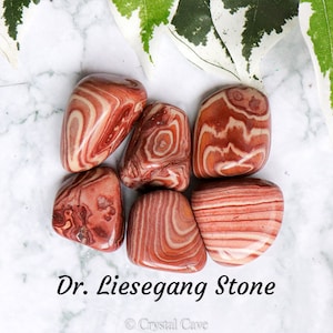 May include: Six tumbled stones of Dr. Liesegang stone, a type of banded agate with red and white stripes. The stones are smooth and polished, and they have a natural, organic look.
