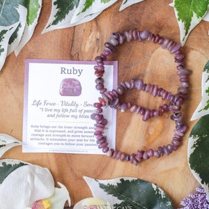 May include: A pink ruby crystal bracelet with a card that reads "Ruby" and "Life Force - Vitality - Sensuality" with the quote "I live my life full of passion and follow my bliss."