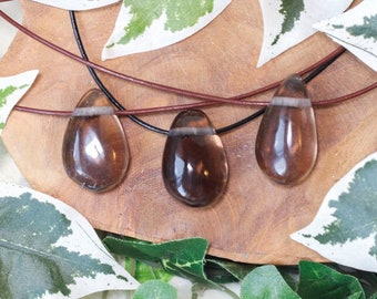 May include: Three smoky quartz teardrop pendants on brown leather cords. The pendants are a light brown color and have a translucent appearance. The cords are tied together in a knot at the top.