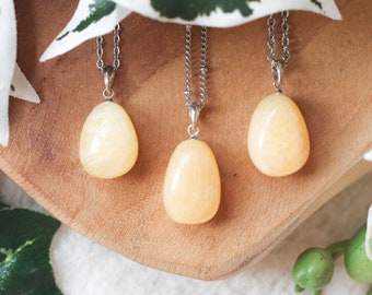 Puede incluir: Tres collares colgantes de calcita amarilla sobre una superficie de madera. Cada collar presenta una piedra lisa en forma de lágrima.