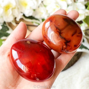 Peut inclure: Deux pierres de carnelienne rouge roulées, l'une avec une teinte rouge plus foncée et l'autre avec une teinte rouge plus claire. Les pierres sont lisses et polies, avec une finition brillante.
