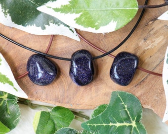 May include: Three dark blue, sparkly, gemstone pendants on a black leather cord necklace. The pendants are teardrop shaped and have a glittery finish.