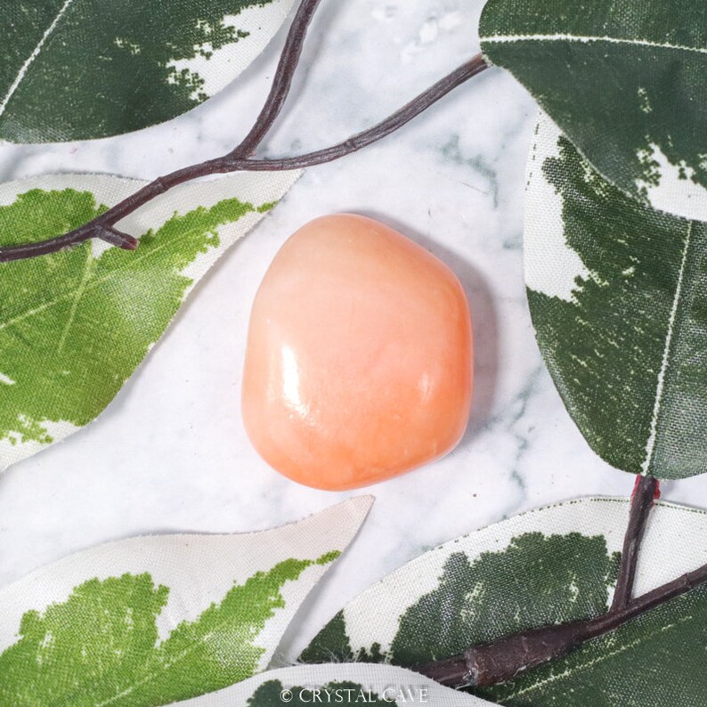 May include: A smooth, polished, peach-colored carnelian stone. The stone is heart-shaped and has a glossy finish.