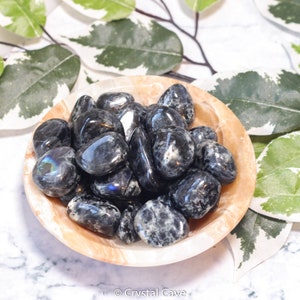 May include: A bowl of black and grey tumbled stones. The stones have a speckled appearance and some have a slight iridescent sheen.