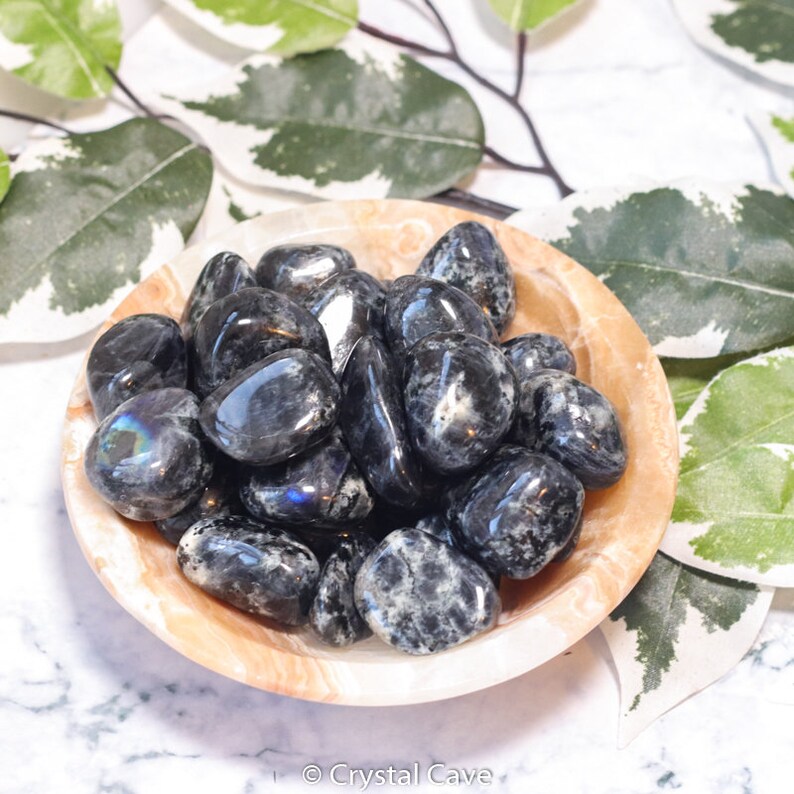May include: A bowl of black and grey tumbled stones. The stones have a speckled appearance and some have a slight iridescent sheen.