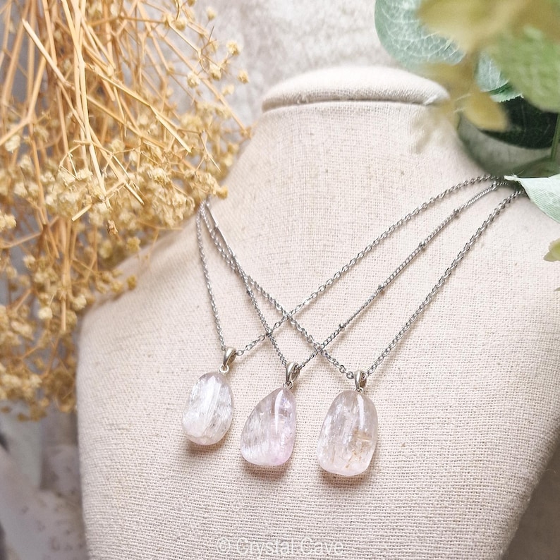 Puede incluir: Tres collares de plata con colgantes de cristal rosa y blanco. Los collares est&aacute;n superpuestos en un busto de maniqu&iacute; blanco.