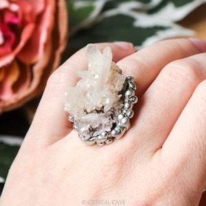 May include: A silver ring with a cluster of white quartz crystals set in a silver bezel. The ring is on a person's finger.