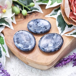 May include: Three smooth, oval-shaped polished stones, each with a unique pattern of grey and blue. The stones are arranged on a wooden surface.
