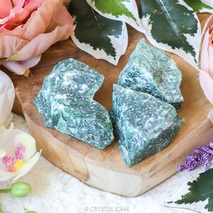 Peut inclure: Quatre gros morceaux de cristal d'aventurine verte sur une surface en bois. Les cristaux sont de couleur vert clair avec un aspect moucheté.