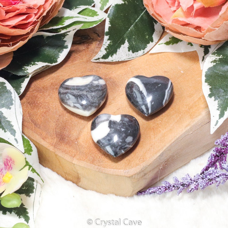 Peut inclure: Trois pierres en forme de c&oelig;ur ray&eacute;es de noir et de blanc sur une surface en bois. Les pierres sont polies et ont un aspect naturel et organique.