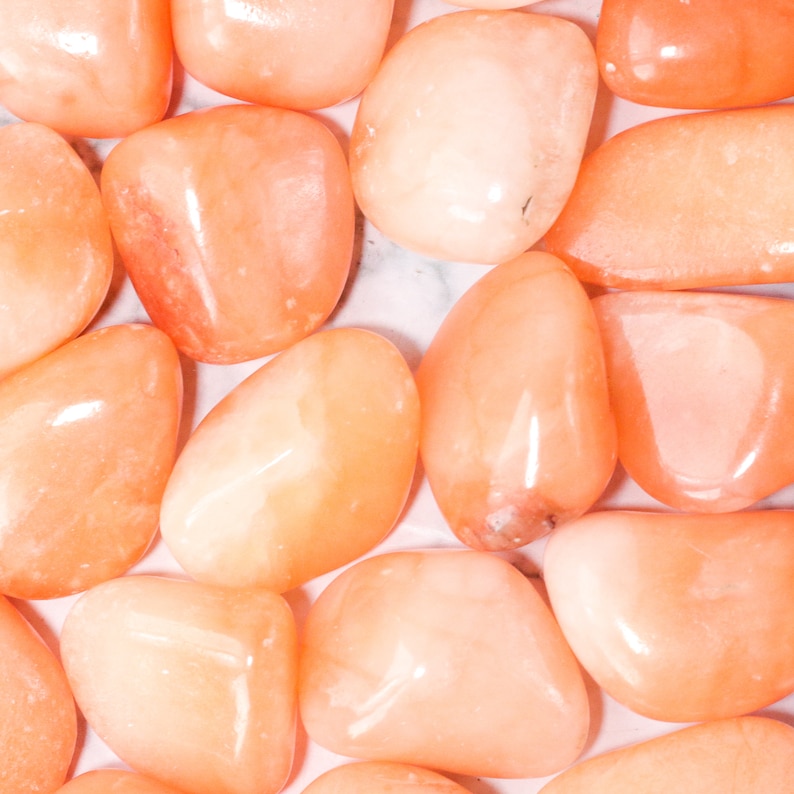May include: A collection of smooth, polished carnelian stones in various shades of orange and peach. The stones are tumbled and have a natural, organic shape.