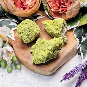 Puede incluir: Tres piedras de musgo verde sobre una superficie de madera. Las piedras tienen una forma irregular y una textura rugosa.