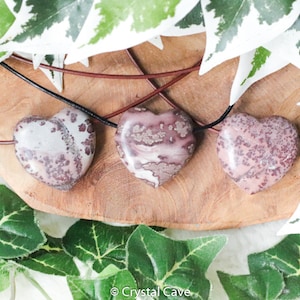 May include: Three pink and white heart-shaped pendants with brown leather cords. The pendants are made of polished stone with a speckled pattern.