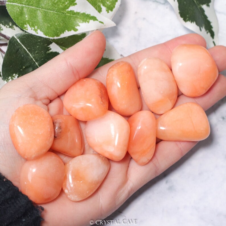 May include: A collection of tumbled carnelian stones in various shades of orange and peach. The stones are smooth and polished, with a natural, earthy look.