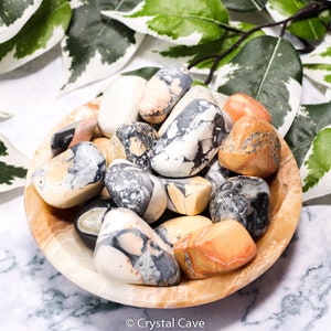 May include: A bowl of tumbled ocean jasper stones. The stones are a mix of white, black, orange, and yellow with swirling patterns.