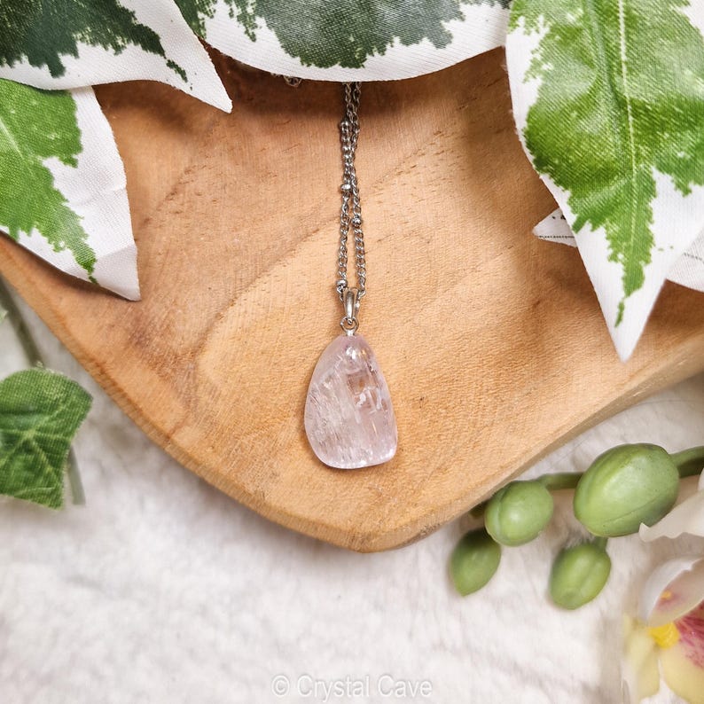 Puede incluir: Un collar de cadena plateada con un colgante de cristal transparente, rosa claro y transl&uacute;cido. El colgante tiene una forma libre y tiene un aspecto natural y en bruto.