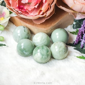 Può includere: Sei sfere di giada verde, ciascuna con un motivo a spirale unico, sono disposte su una superficie bianca. Le sfere sono lisce e lucidate, con un bagliore sottile.