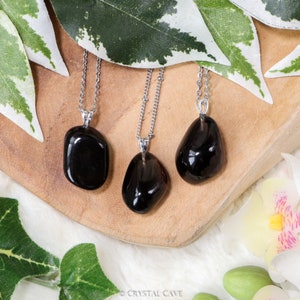 May include: Three silver necklaces with black gemstone pendants. The pendants are smooth and oval-shaped. The necklaces are displayed on a wooden surface.