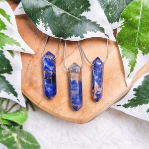 Puede incluir: Tres colgantes de piedra azul y marrón en cadenas de plata. Los colgantes son todos puntiagudos en la parte superior y tienen un acabado liso y pulido.