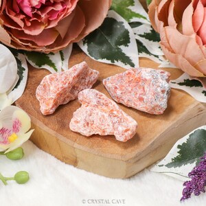 May include: Three orange calcite crystal clusters on a wooden surface. The crystals are rough and have a white, cloudy appearance.