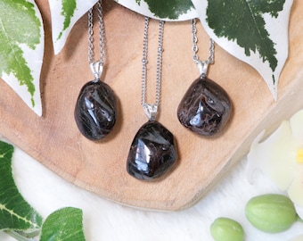 May include: Three silver necklaces with dark brown gemstone pendants. The pendants are irregularly shaped and have a shiny, polished finish.