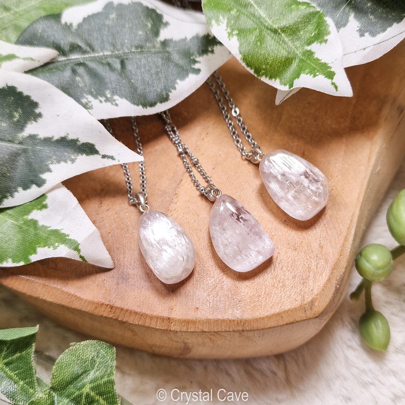Puede incluir: Tres collares de plata con colgantes de cristal transparente y blanco en forma de l&aacute;grima. Los collares se muestran sobre una superficie de madera con hojas verdes en el fondo. &copy; Crystal Cave