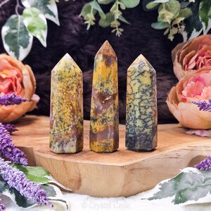 May include: Three yellow, brown, and white banded agate crystal points on a wooden surface. The points are polished and have a natural, organic look.